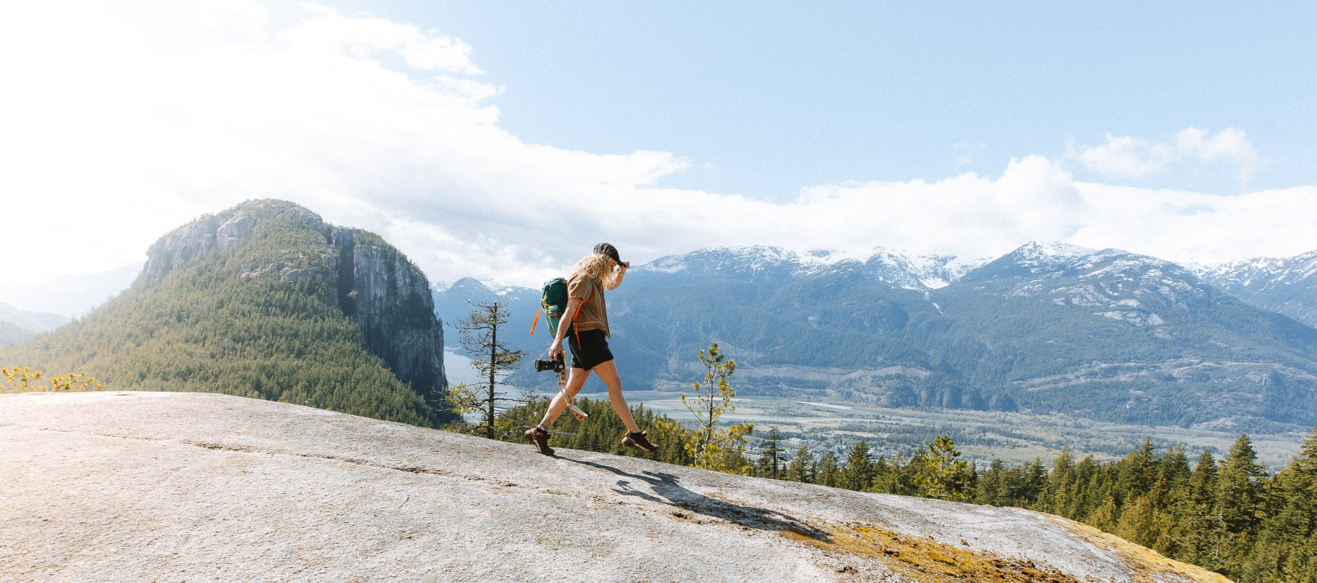 A woman wearing shorts walking along a mountain ridge with snowy peaks in the background