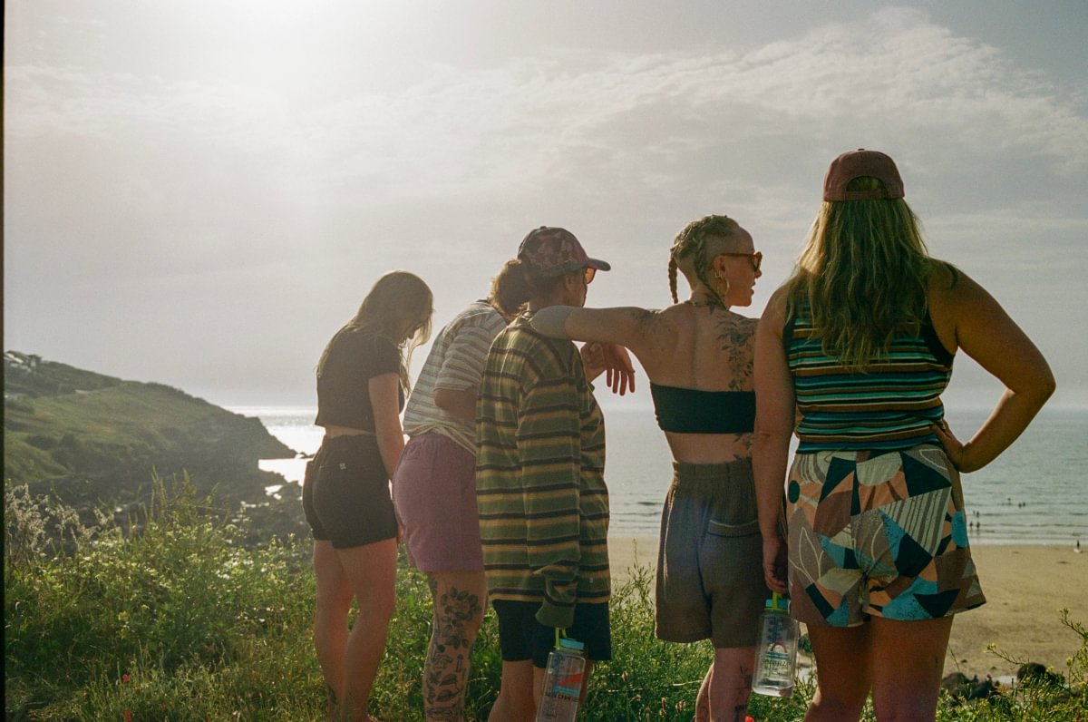 5 women standing on a cliff edge overlooking the ocean at golden hour